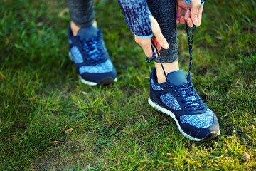Woman in sportswear tying shoelaces on sneakers outdoor close-up