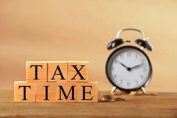 Tax concept with wooden cubes, coins and alarm clock on light background