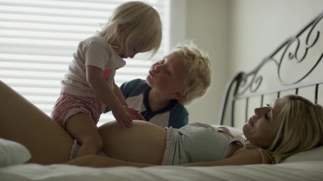 Medium slow motion shot of pregnant mother playing with children on bed / Cedar Hills, Utah, United States