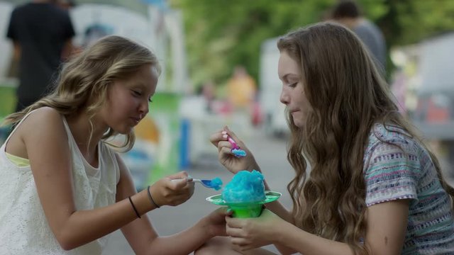 Slow motion medium shot of girls eating shaved-ice at funfair / Pleasant Grove, Utah, United States