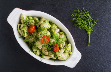 Broccoli pasta (shell shape) with dill and spices in baking dish on dark stone background. Top view.