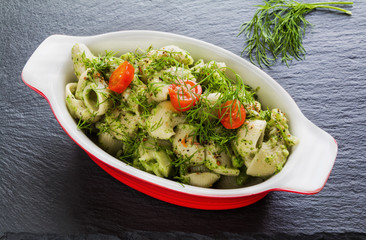 Broccoli pasta (shell shape) with dill and spices in baking dish on dark stone background.