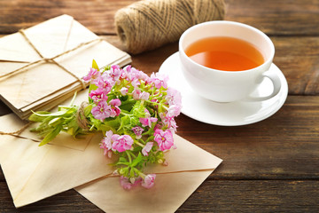 Bouquet of meadow flowers with tea and envelopes on wooden table