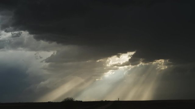 Time-lapse dark cloud and sun rays moving to the right across the prairie at dusk