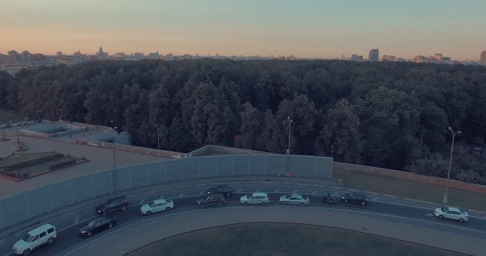 Aerial view of city traffic, road, public park, tops of the trees, Moscow River, and city skyline during sunset in Moscow, Russia.