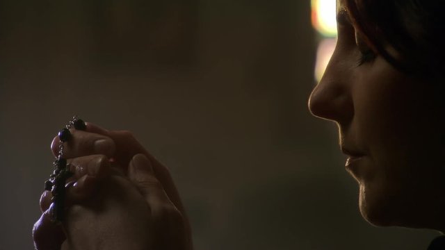 Close-up of praying woman's face, left pan to rosary in hands