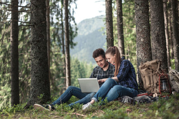 Fototapeta premium A couple of tourists sitting and looking at laptop in the woods. The concept of active rest