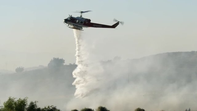 A helicopter drops a load of water into the smoke of a fire