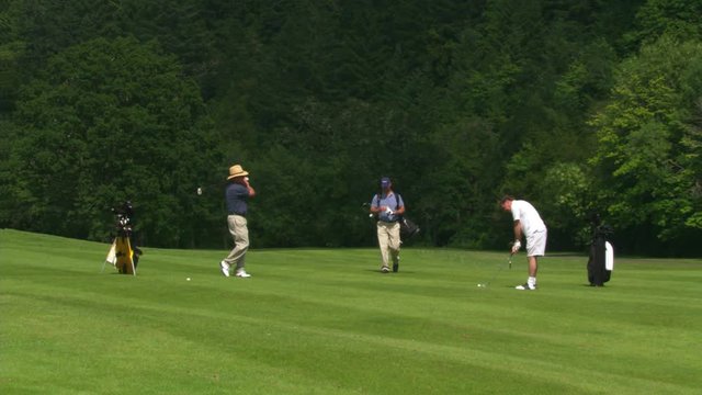 Three men following up balls on a golf course fairway