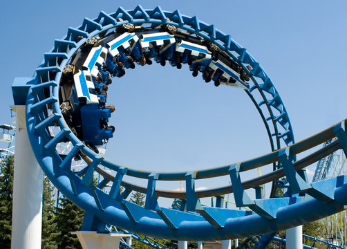 Cork-screw Rollercoaster and Ferris-Wheel at amusement park. Slight motion blur on Rollercoaster cars