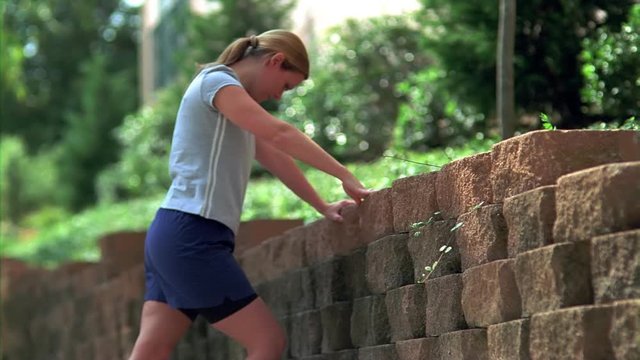 Young woman leaning on stone wall, stretching leg muscles