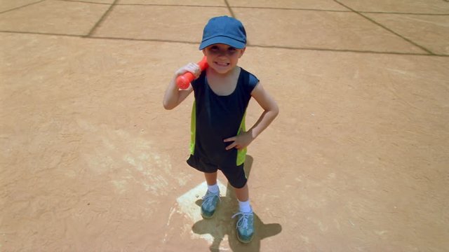 Little boy with orange ball bat posing on a paved play area, angled view