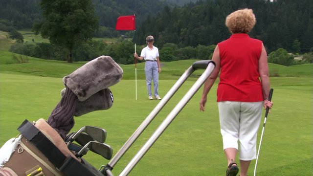 Woman golfer making a putt while female companion holds flag stick; ball runs past hole