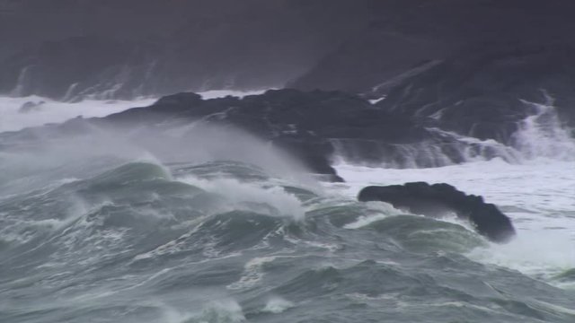 Tossing waves pounding the base of dark seacliffs on a rocky headland