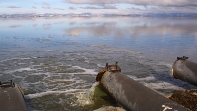Three drainpipes, one discharging greenish water into Tule Lake