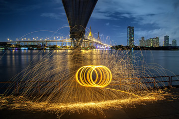 Hot Golden Sparks Flying from Man Spinning Burning Steel Wool under Bhumibol Bridge in Bangkok...