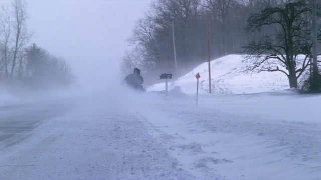 Snowmobilers racing along snow-packed rural highway between drifts