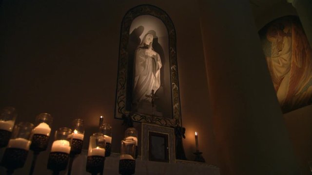 Statue of the Virgin Mary in wall niche, camera dollies past candles and pillar