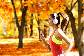 Young beautiful woman running in autumn park and listening to music with headphones.