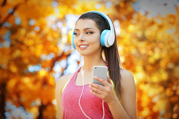 Young beautiful woman running in autumn park and listening to music with headphones.