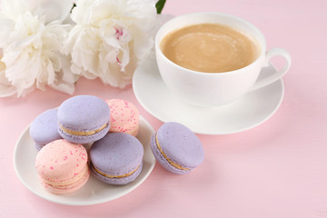 Cup of coffee with macaroons and peonies on pink background