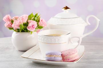 Cup of tea with macaroons and roses on wooden table