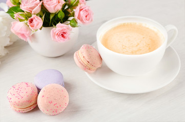 Cup of coffee with macaroons and roses on wooden table