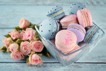 Tasty macaroons with beautiful roses on wooden table
