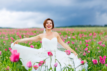 Fototapeta na wymiar happy bride in white dress having fun in flower poppy field 