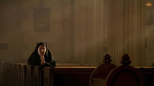 Praying nun kneeling among sun rays in empty church