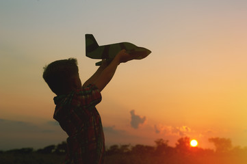 Happy kid playing with toy airplane on sunset background