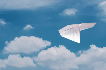 Paper plane flying over clouds with blue sky.