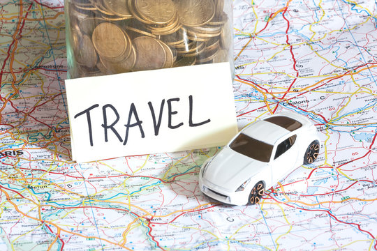 Closeup of coins in a jar with travel sign and a toy car on a ma