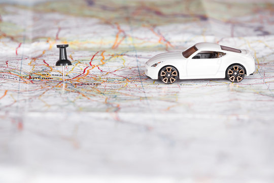 White toy car with a black pin on a map. Shallow depth of field.