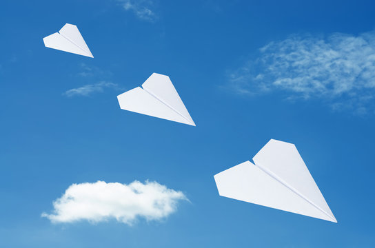 Paper plane flying over clouds with blue sky.
