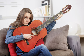 Fototapeta premium Happy girl playing guitar at home in living room, smiling.
