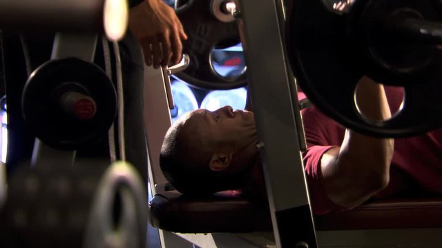 Man lying on bench in weight room and pressing heavily weighted bar