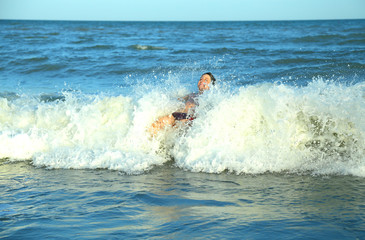 Naklejka premium happy boy plays by jumping the waves of the sea