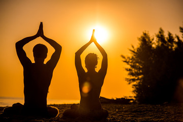 An attractive young woman and man doing yoga on the beach, Sea