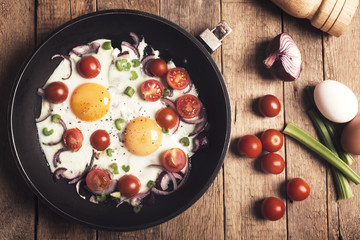 Fried eggs with vegetables on the rustic wooden table