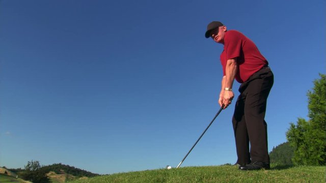 Golfer skylined on hilltop, swing spraying sand and turf toward camera