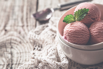 Raspberry ice cream in white bowl, rustic wood background