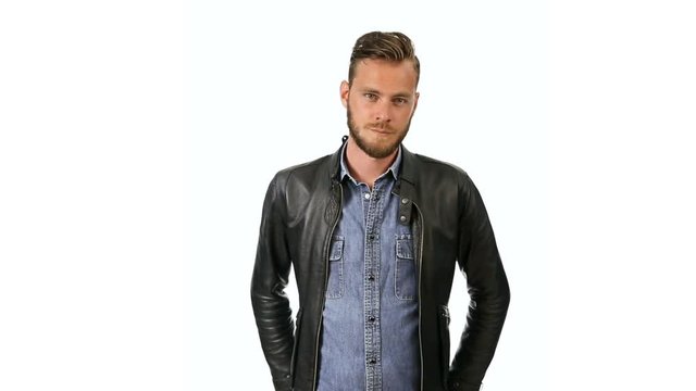 A fashionable man wearing a jeans shirt with a black leather jacket standing against a white background looking at camera.