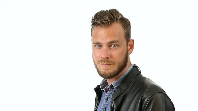 A fashionable man wearing a jeans shirt with a black leather jacket standing against a white background looking at camera.