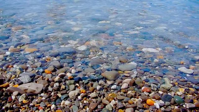 Pebble beach with small pebbles and sea surf. The surface of the sea on a wild pebble beach. The waves are to the camera. The view under water. Wave foam.