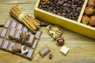 Still life with a delicious chocolate bar,cinnamon,roasted coffee beans,sugar and nuts on a wooden table,top view