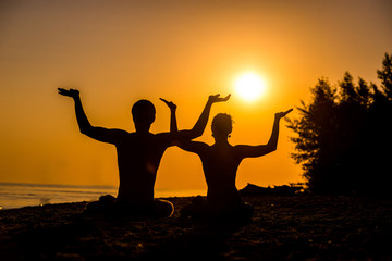 Fototapeta na wymiar An attractive young woman and man doing yoga on the beach, Sea