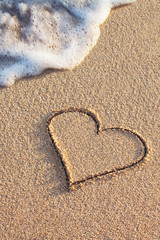 Fototapeta na wymiar heart symbol handwritten on sandy beach with soft ocean wave