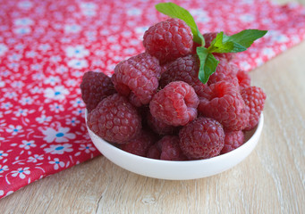 Red raspberries in white plate on gbeige wooden background, a bright red background