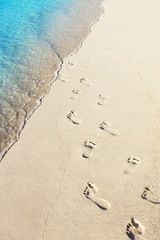 Foot prints on a sandy beach with blue ocean wave on background
